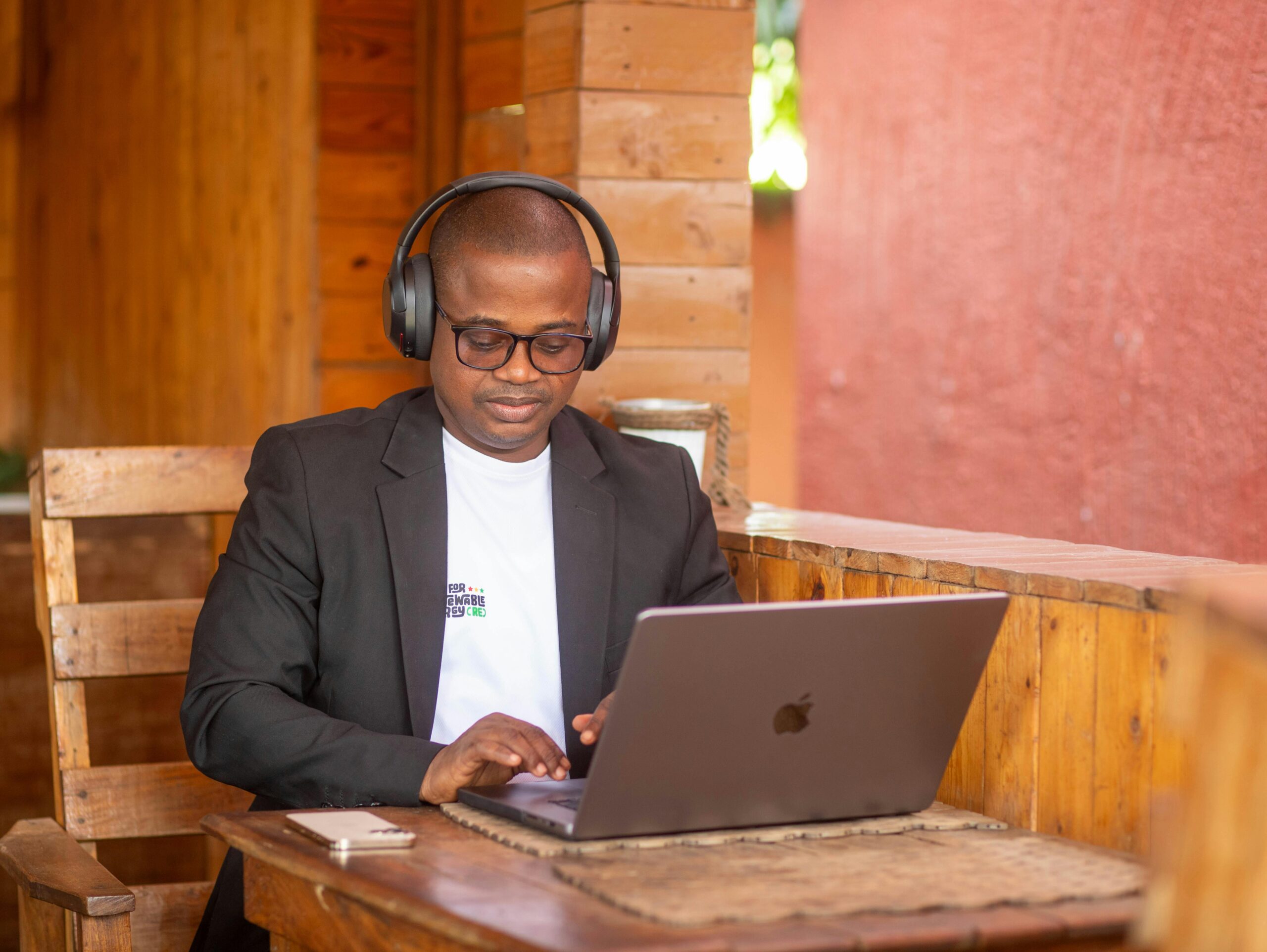 Ein konzentrierter Mann arbeitet in einem gemütlichen Café mit Kopfhörern an seinem Laptop.